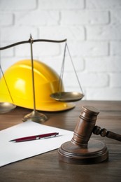 Photo of Labour, construction and land law concepts. Judge gavel, scales of justice, protective helmet, paper sheet with pen on wooden table