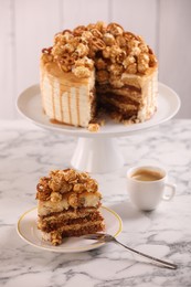 Photo of Caramel drip cake decorated with popcorn and pretzels served on white marble table