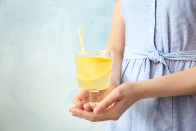 Young woman holding glass with lemon cocktail against color background