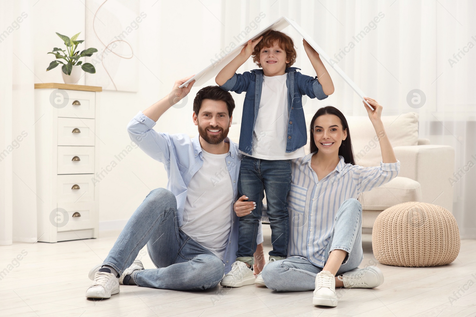 Photo of Housing concept. Happy family holding plastic roof on floor at home