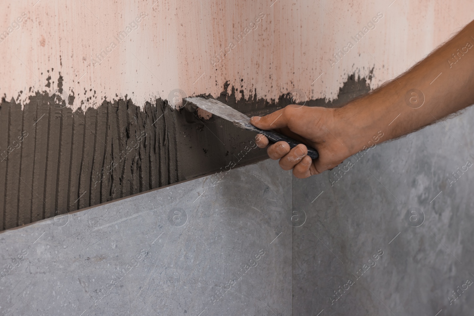 Photo of Worker spreading adhesive mix on wall, closeup. Tiles installation process