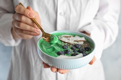 Photo of Woman eating tasty spirulina smoothie with blueberries, coconut and chia seeds, closeup