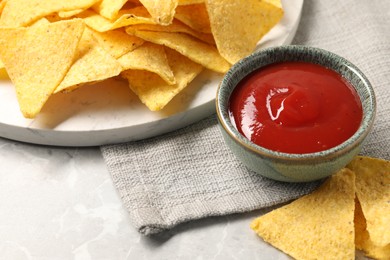 Photo of Tasty ketchup and tortilla chips on grey table, closeup