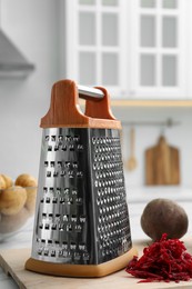 Grater and fresh ripe beetroot on table in kitchen