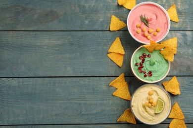 Different kinds of tasty hummus served with nachos on light blue wooden table, flat lay. Space for text