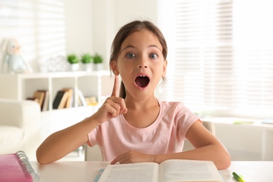 Photo of Emotional little girl doing homework at table indoors