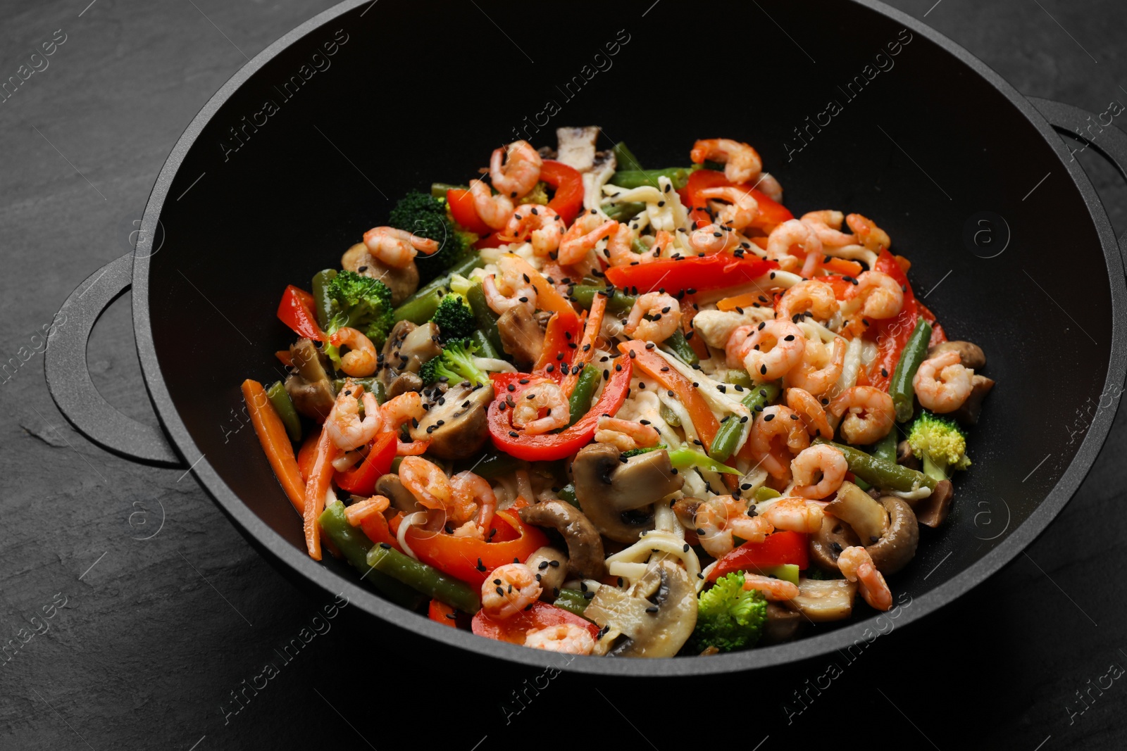 Photo of Stir fried noodles with mushrooms, shrimps and vegetables in wok on black table, closeup