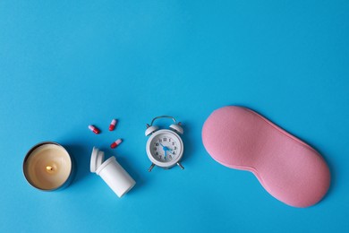 Photo of Sleeping mask, pills, candle and alarm clock on light blue background, flat lay. Insomnia treatment