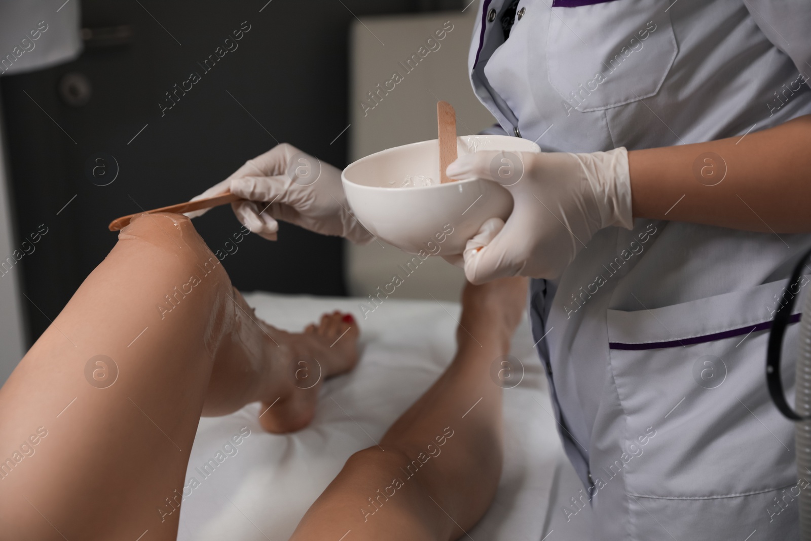 Photo of Professional cosmetologist applying gel on client's leg before laser epilation procedure in salon, closeup