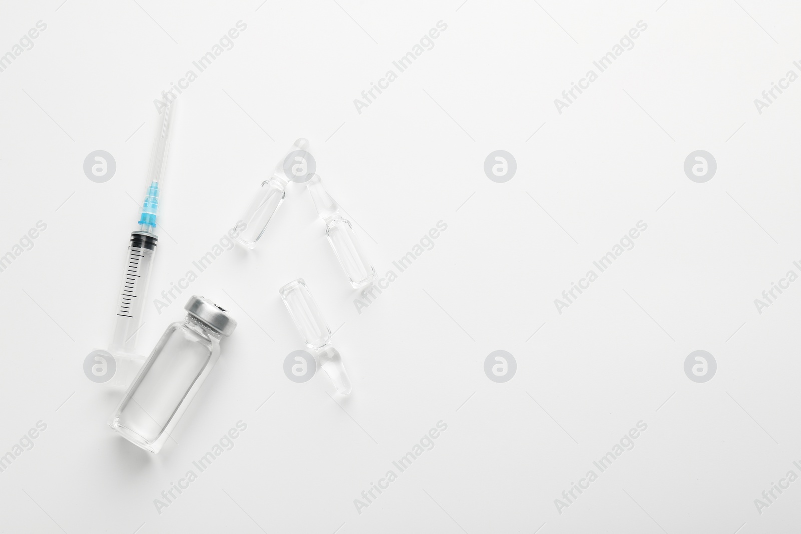 Photo of Glass ampoules with liquid and syringe on white background, flat lay. Space for text