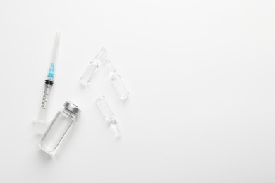 Photo of Glass ampoules with liquid and syringe on white background, flat lay. Space for text