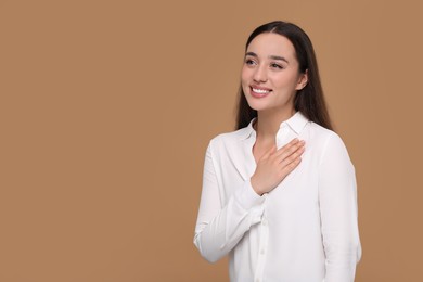 Photo of Thank you gesture. Beautiful grateful woman with hand on chest against brown background, space for text