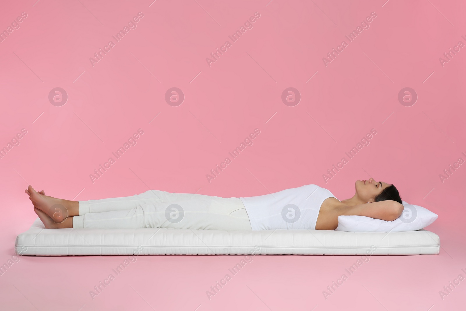 Photo of Young woman lying on soft mattress against pink background