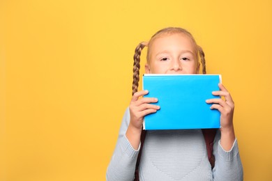 Photo of Cute little girl with textbooks on yellow background. Space for text