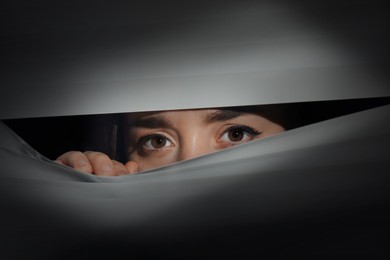 Image of Worried woman looking through window blinds into darkness. Paranoia concept