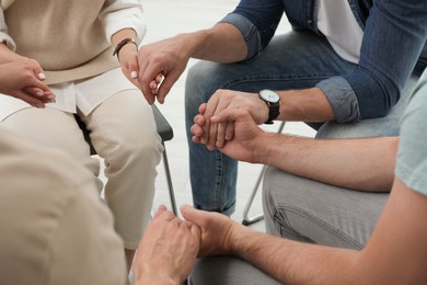 Psychotherapist and group of drug addicted people holding hands together at therapy session, closeup