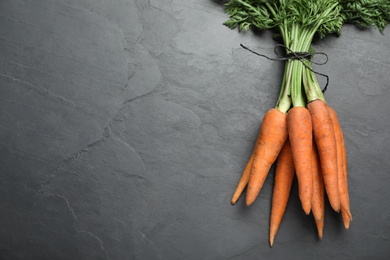 Photo of Bunch of tasty raw carrots on black slate table, top view. Space for text