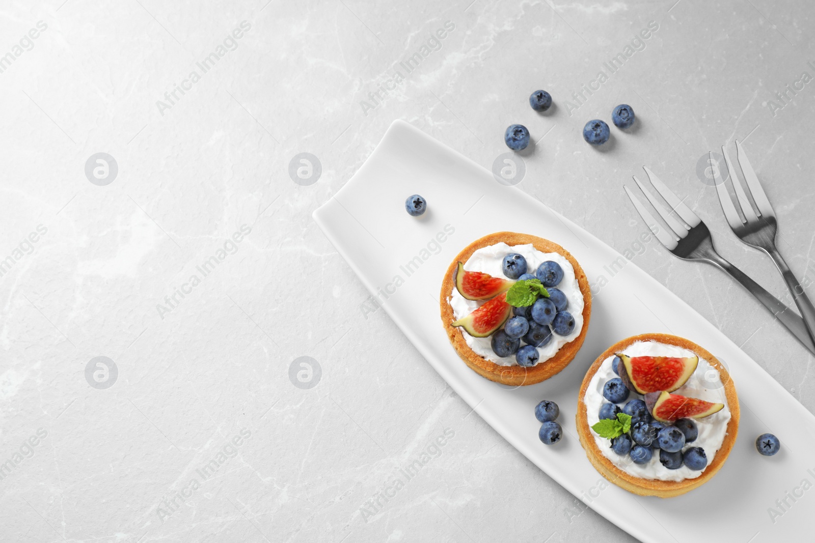 Photo of Tarts with blueberries and figs on marble table, flat lay with space for text. Delicious pastries