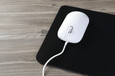 Wired mouse and mousepad on wooden table, space for text