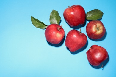 Photo of Ripe red apples and green leaves on light blue background, flat lay. Space for text