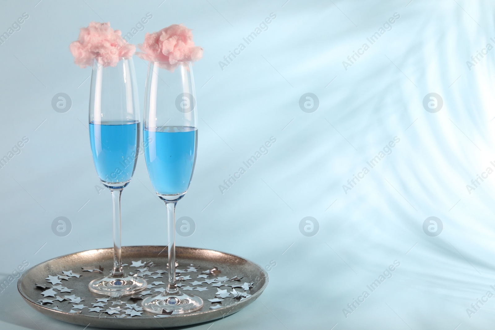 Photo of Cotton candy cocktails in glasses and confetti on light blue background, space for text