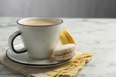 Tasty cappuccino in cup, macarons and saucer on white marble table, closeup. Space for text