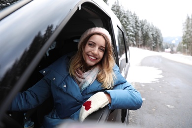 Photo of Young woman driving car and looking out of window on road. Winter vacation