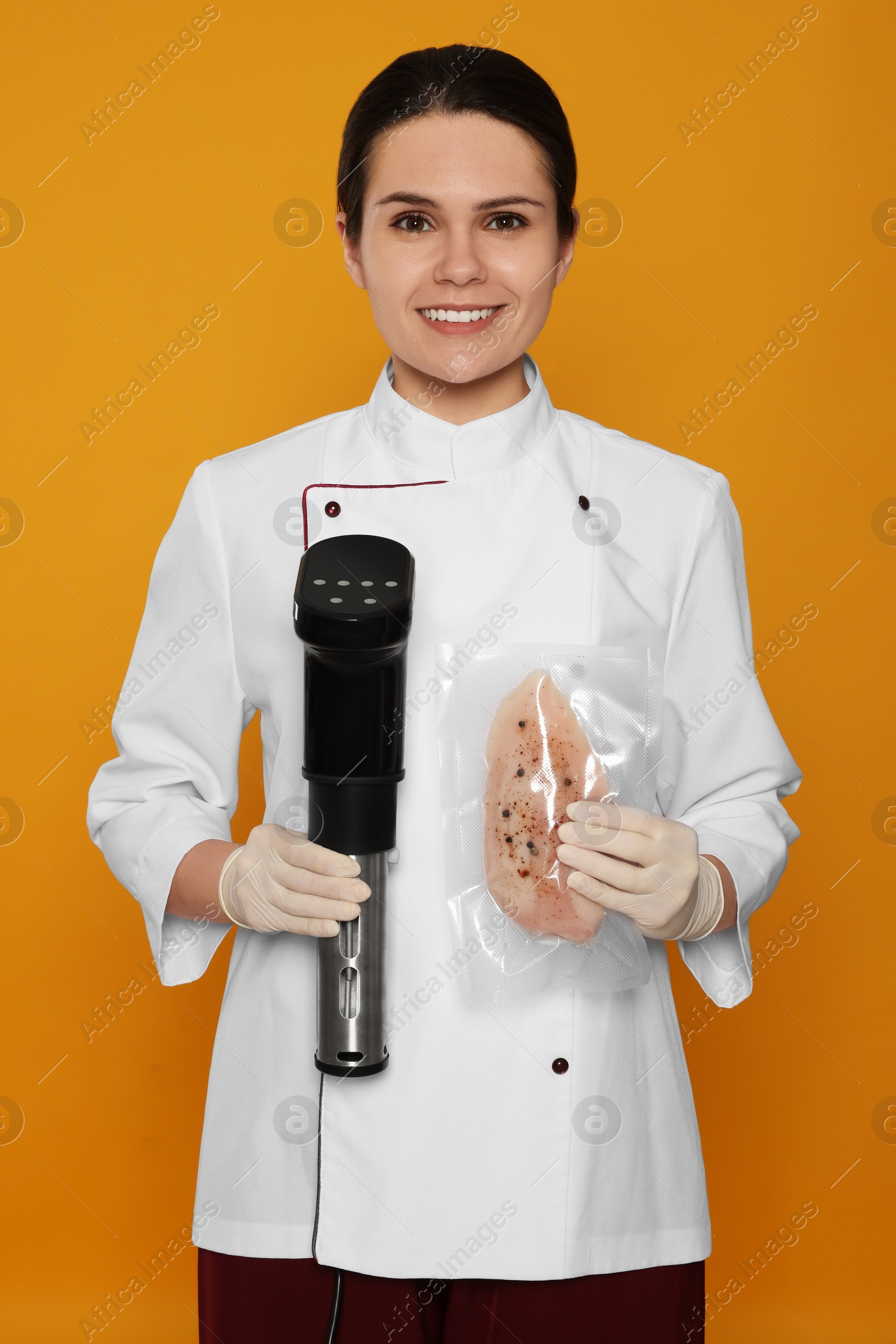 Photo of Chef holding sous vide cooker and meat in vacuum pack on orange background