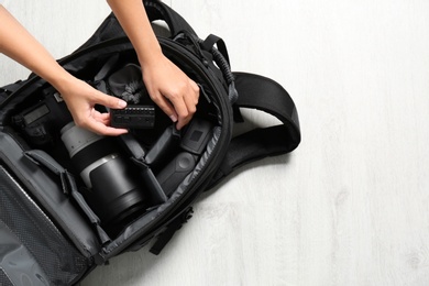 Photo of Woman putting professional photographer's equipment into backpack on floor, top view. Space for text