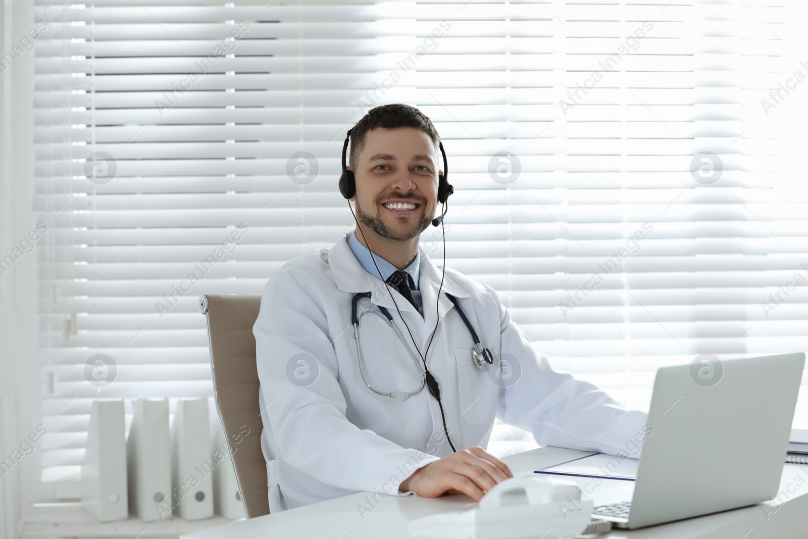 Photo of Doctor with headset sitting at desk in clinic. Health service hotline