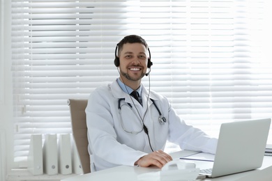 Photo of Doctor with headset sitting at desk in clinic. Health service hotline