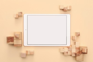 Modern tablet and wooden cubes on beige background, flat lay. Space for text