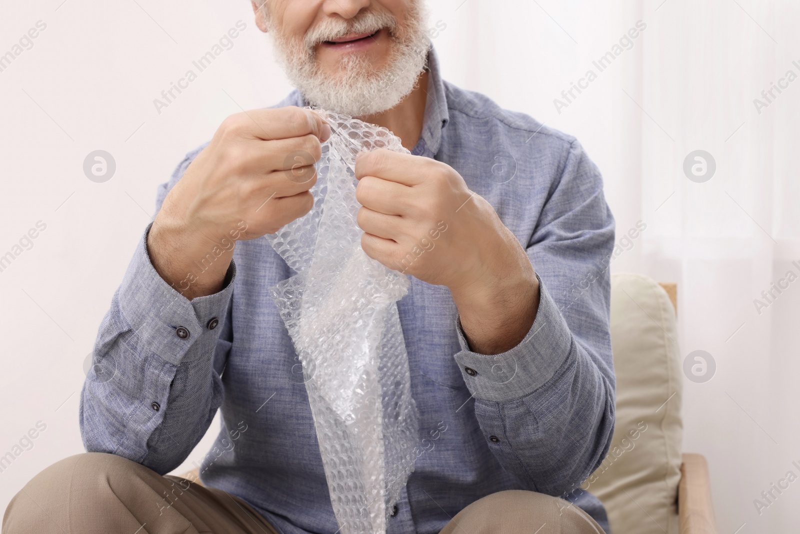 Photo of Senior man popping bubble wrap at home, closeup. Stress relief