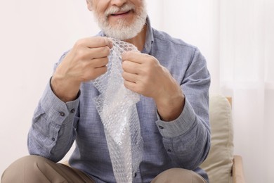 Photo of Senior man popping bubble wrap at home, closeup. Stress relief