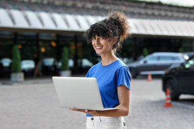 Happy young woman using modern laptop on city street