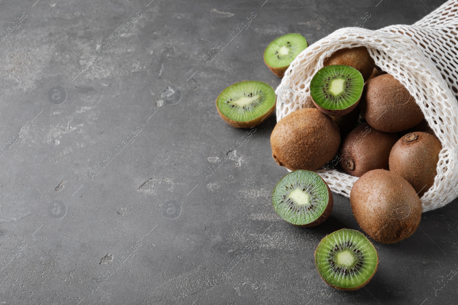 Photo of Net bag with fresh ripe kiwis on grey table, space for text