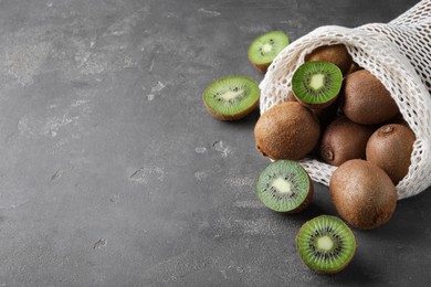 Net bag with fresh ripe kiwis on grey table, space for text