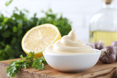 Photo of Tasty mayonnaise sauce in bowl, parsley, garlic and lemon on wooden board, closeup