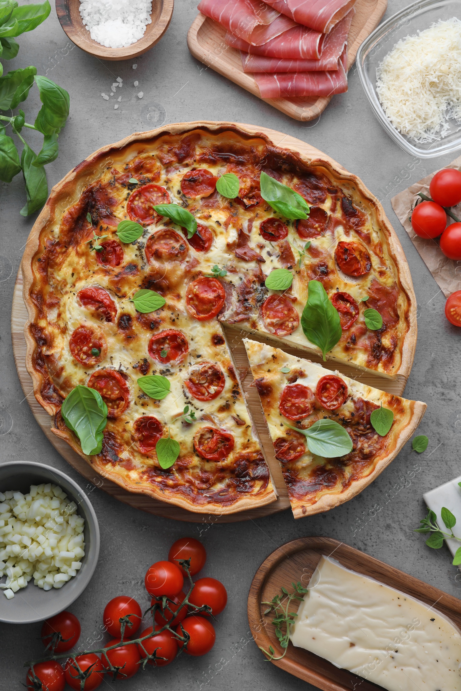 Cut delicious homemade quiche with prosciutto and ingredients on light grey table, flat lay Photo of Cut delicious homemade quiche with prosciutto and ingredients on light grey table, flat lay