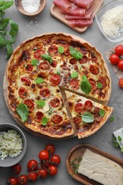 Photo of Cut delicious homemade quiche with prosciutto and ingredients on light grey table, flat lay