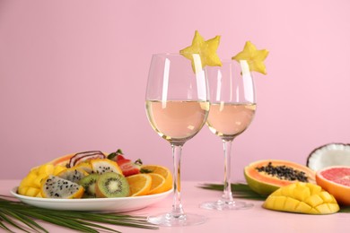 Delicious exotic fruits and glasses of wine on pink wooden table