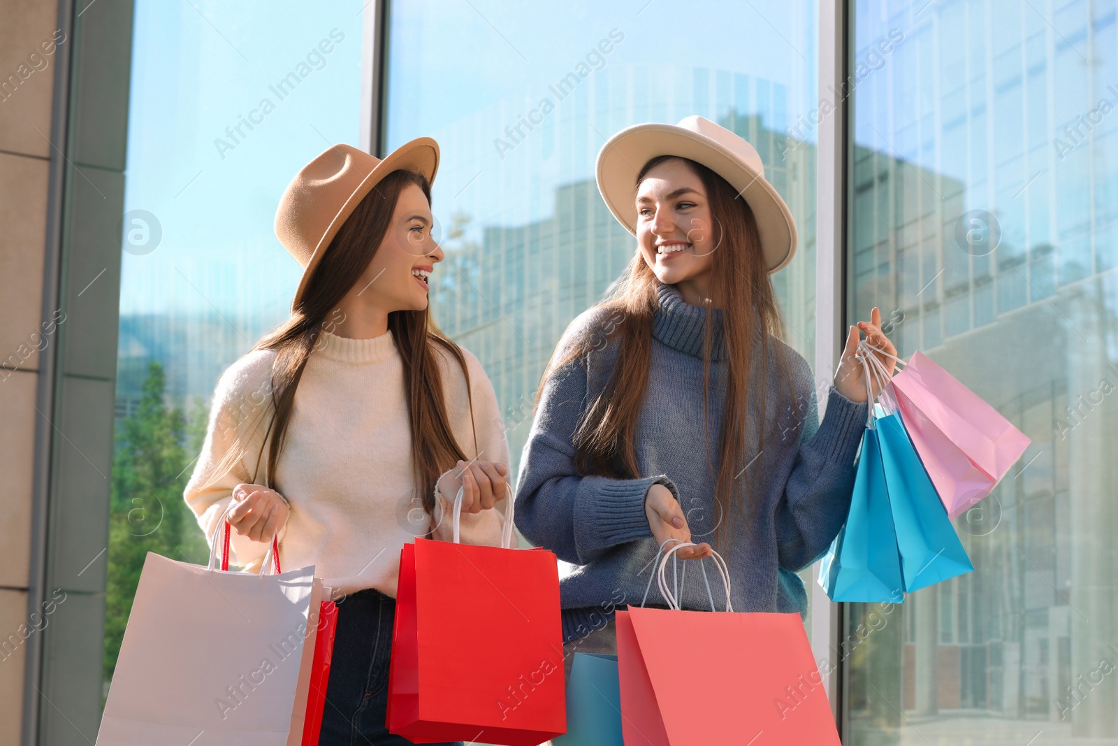 Photo of Beautiful young women with shopping bags near building outdoors