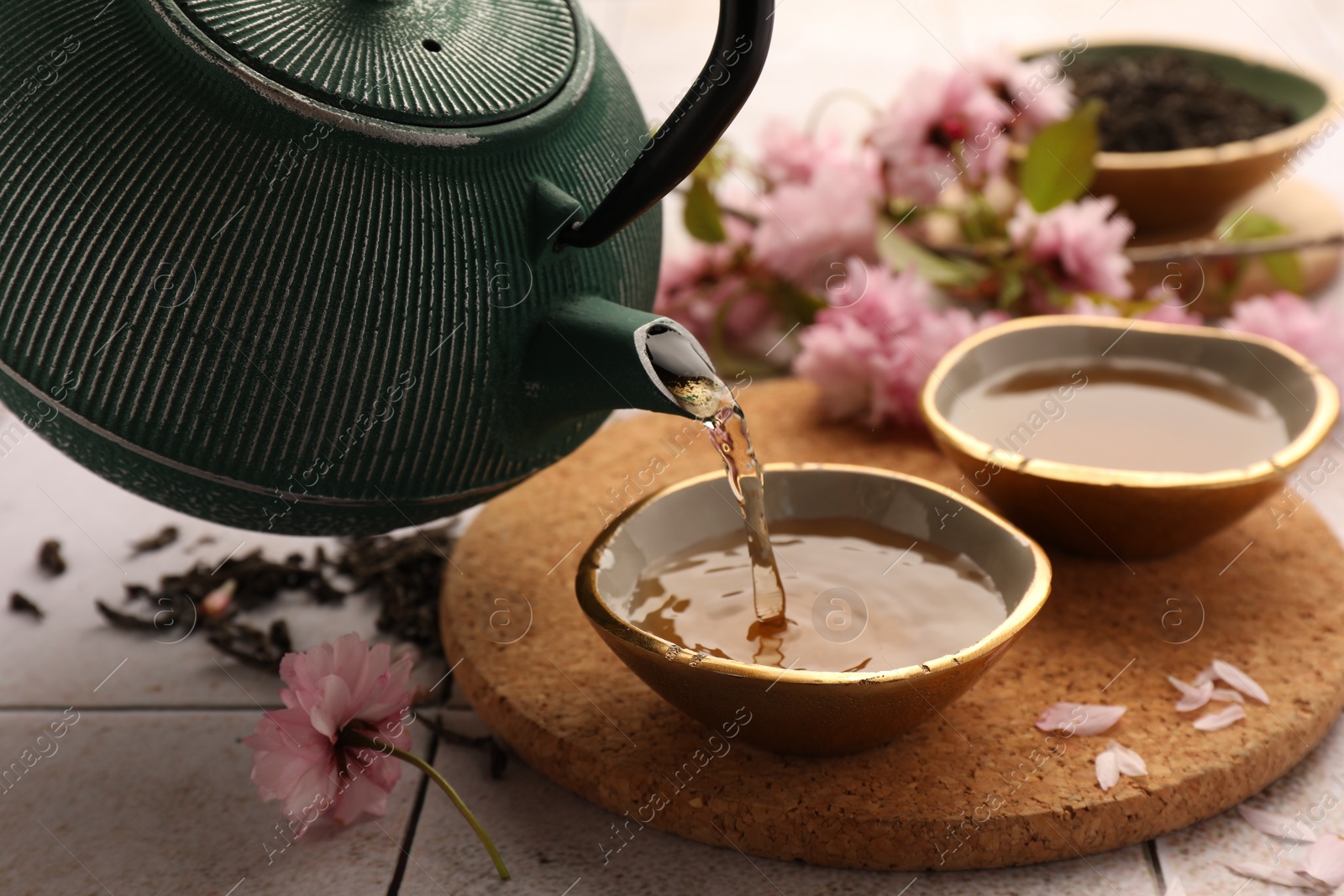 Photo of Traditional ceremony. Pouring brewed tea from teapot into cup on tiled table, closeup