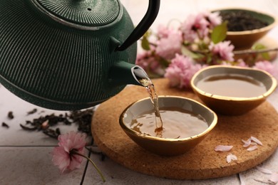 Photo of Traditional ceremony. Pouring brewed tea from teapot into cup on tiled table, closeup