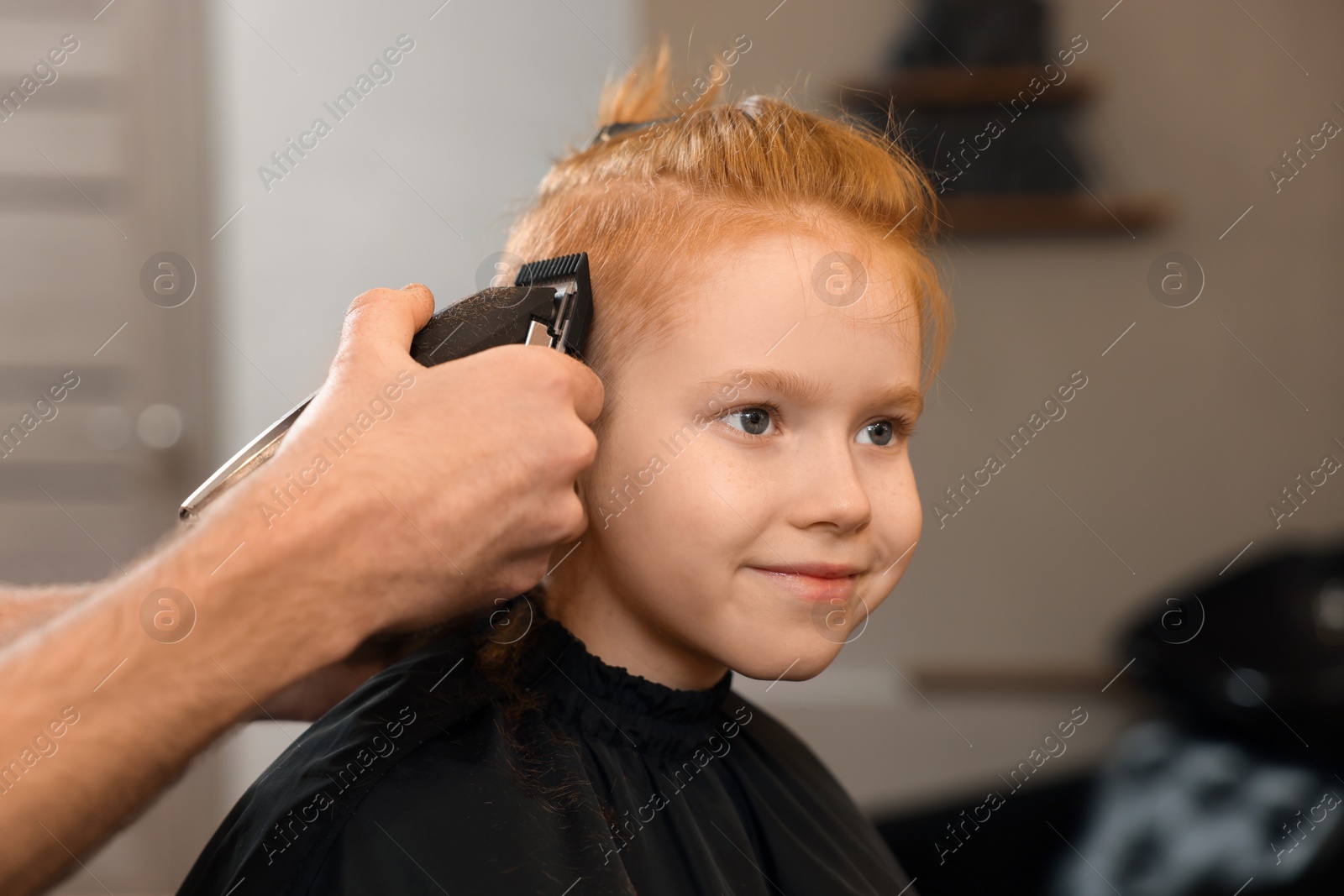 Photo of Professional hairdresser cutting boy's hair in beauty salon, closeup