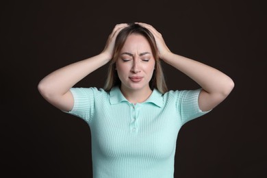 Photo of Young woman suffering from headache on dark brown background