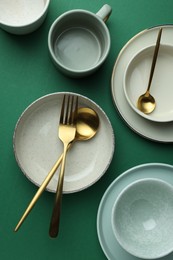 Stylish empty dishware and golden cutlery on green background, flat lay