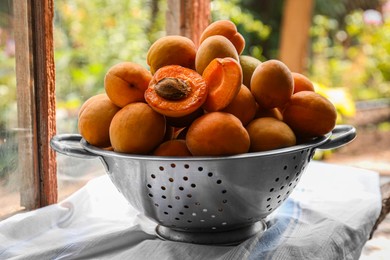 Photo of Colander with delicious ripe apricots on table near window