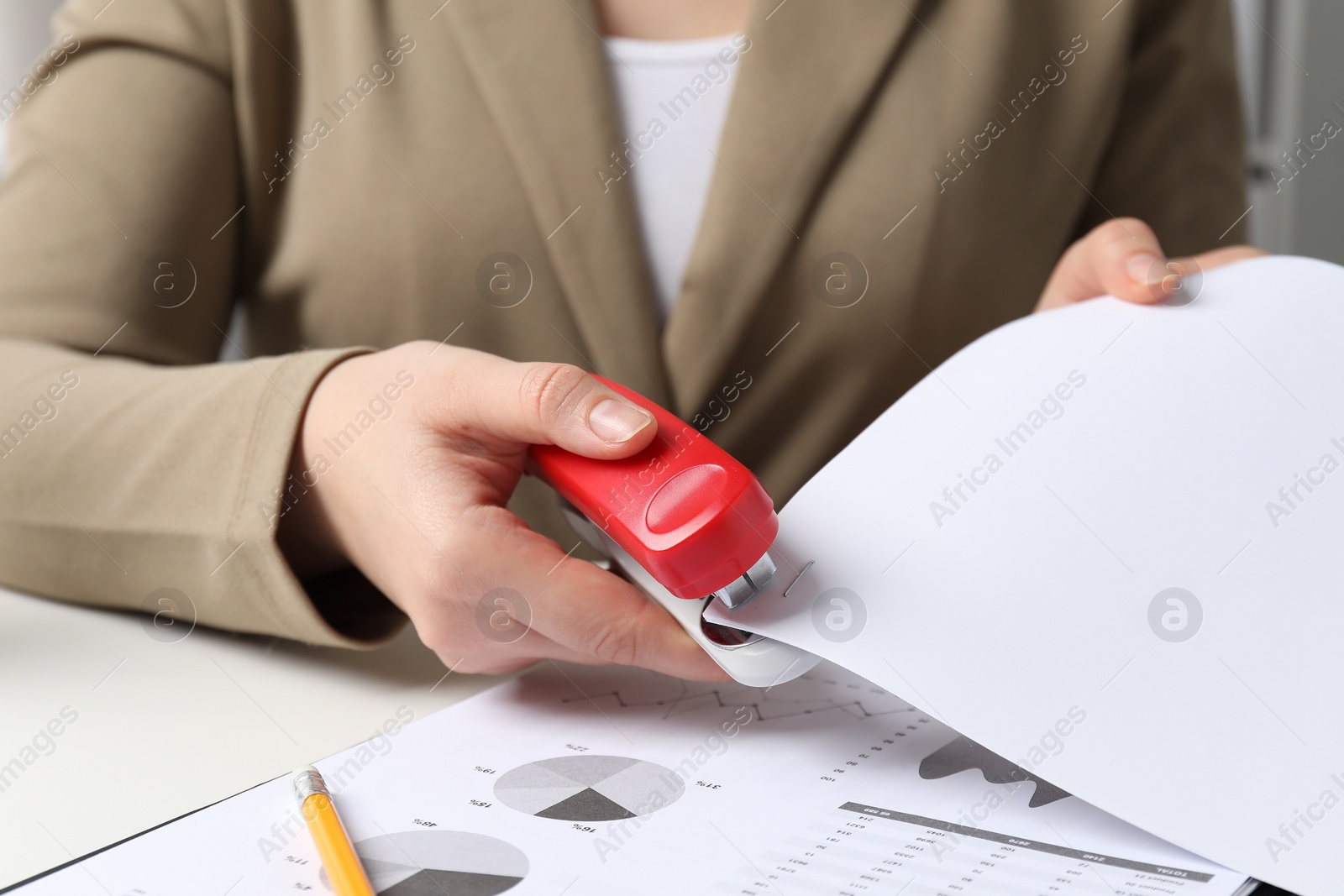 Photo of Woman with papers using stapler at white table, closeup