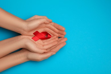 Photo of Woman and girl holding red ribbon on blue background, top view with space for text. AIDS disease awareness